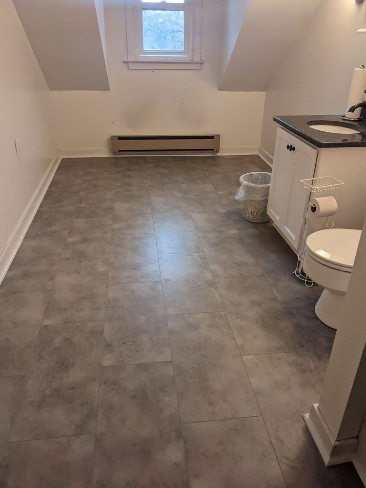 Bathroom with gray flooring, a toilet, a vanity, a window, and a wall-mounted heater.