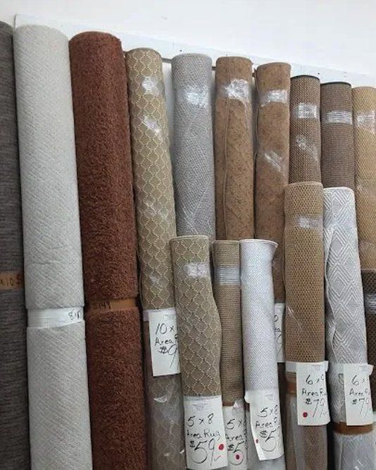 Rolled-up carpets in various colors and textures, stacked vertically against a wall.