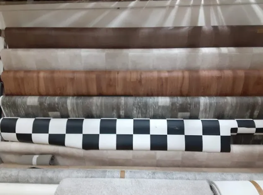 Rolls of flooring samples in various colors and patterns, displayed on shelves.