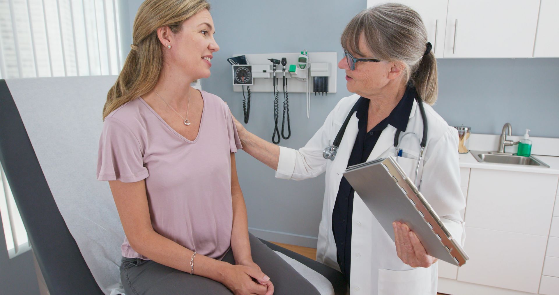 Doctor speaking with a patient during a routine exam while reviewing notes on a clipboard.