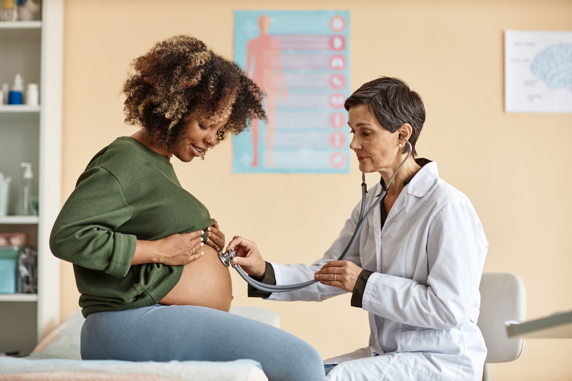 Doctor using a stethoscope to check a pregnant patient’s belly during a prenatal exam.