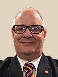A man wearing glasses and a suit and tie is smiling for the camera.