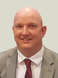 A bald man in a suit and tie is smiling for the camera.