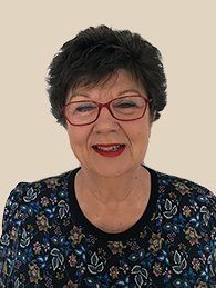 A woman wearing glasses and a floral shirt is smiling.