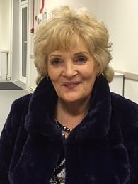 A woman in a blue fur coat is smiling for the camera.