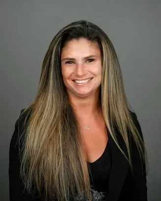 Smiling woman with long blonde hair wearing a black top against a gray background