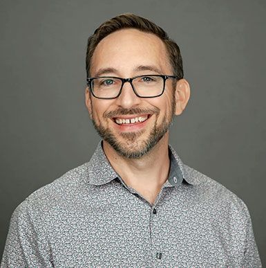 Smiling man with glasses in a patterned shirt against a gray background