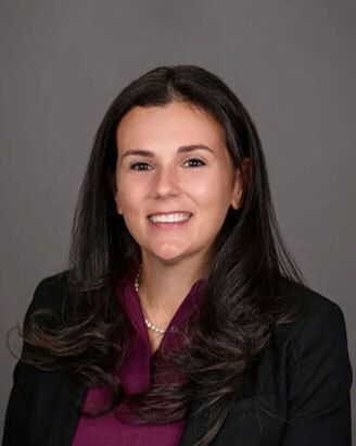Studio portrait of a smiling woman in a black blazer and burgundy blouse on a gray background