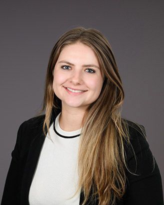 Smiling woman in a black blazer and white top against a gray background