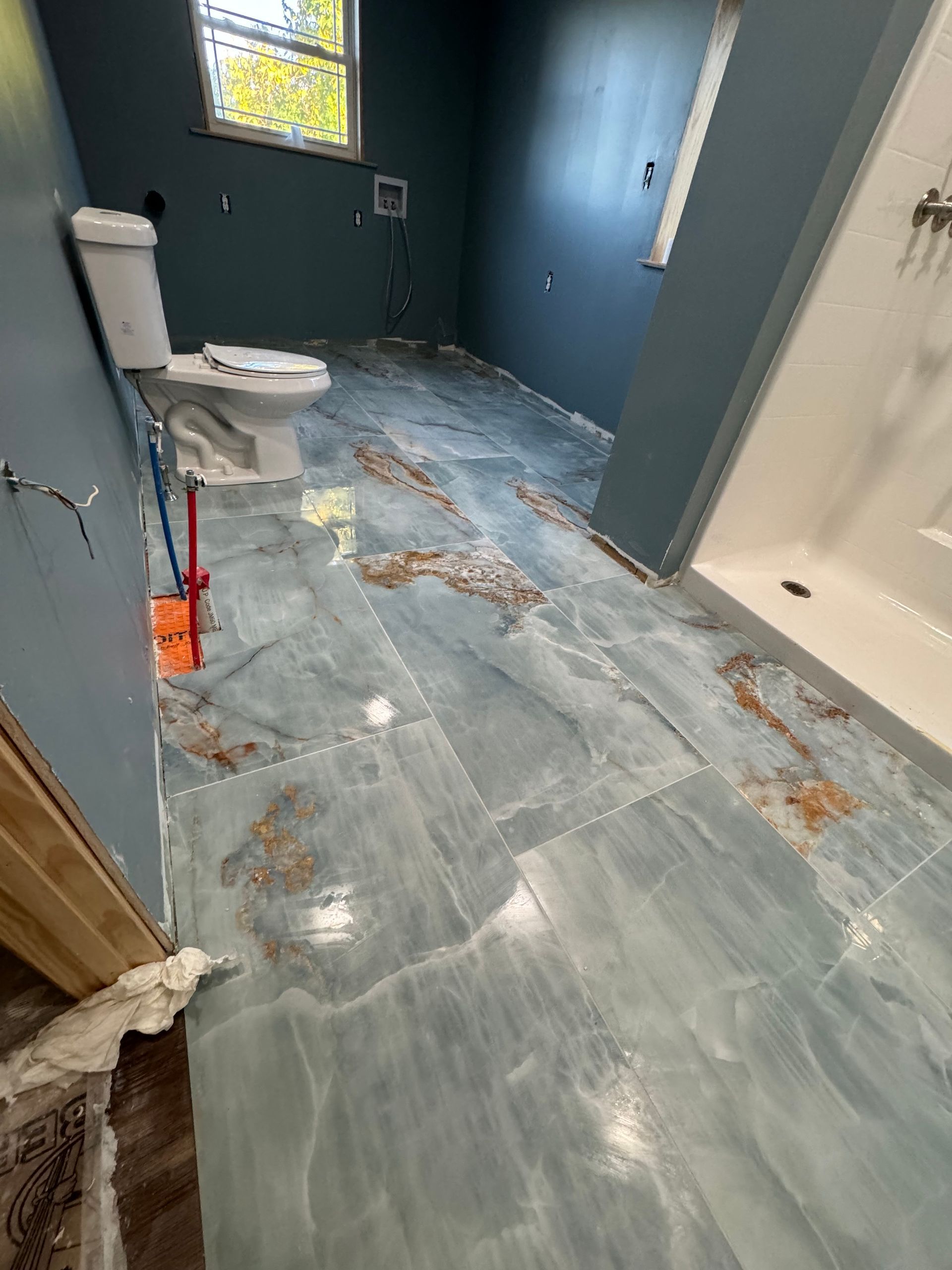 A bathroom with a toilet , shower , and blue tile floor.