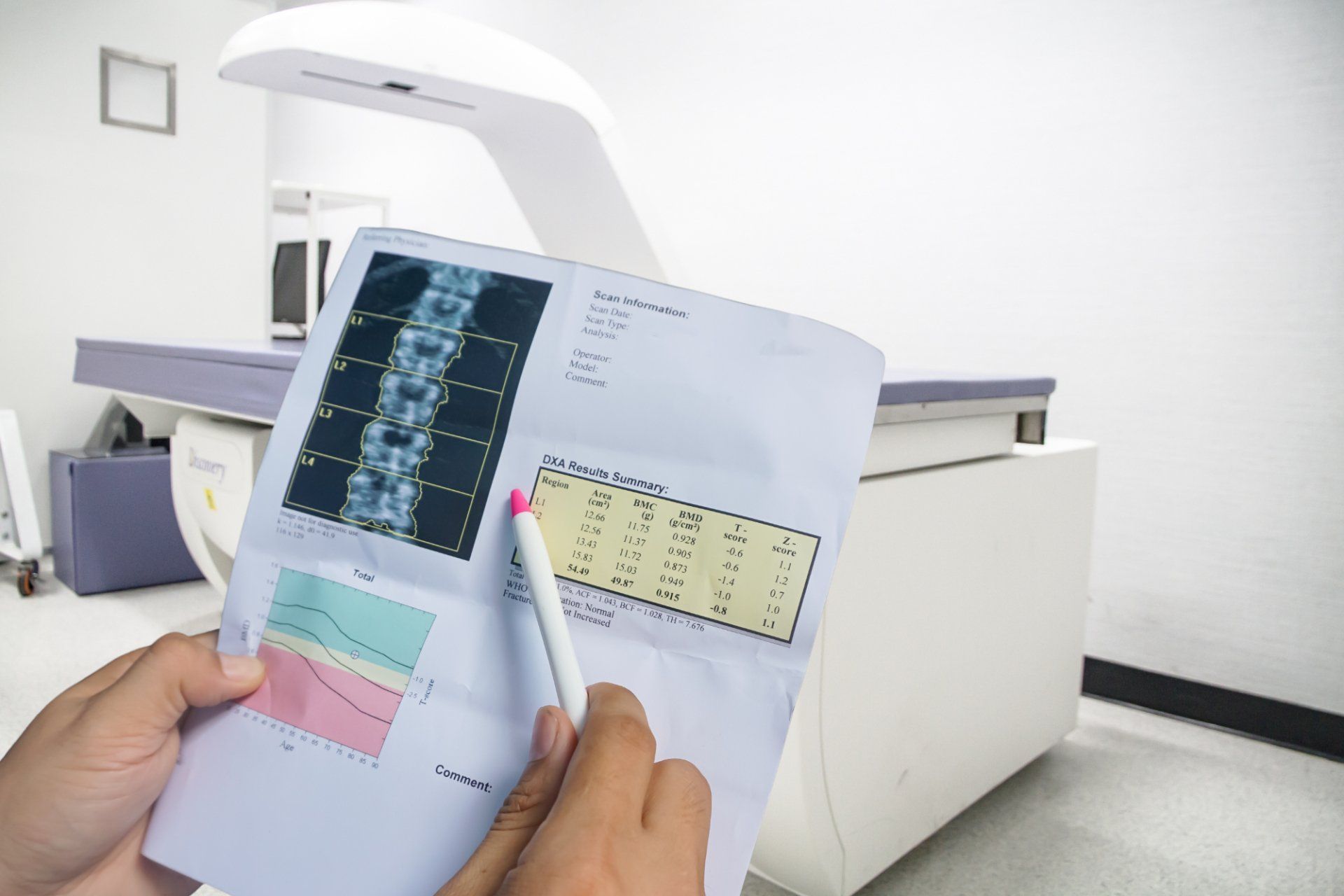 Person examining a bone density scan report with a pen; medical imaging machine in background.