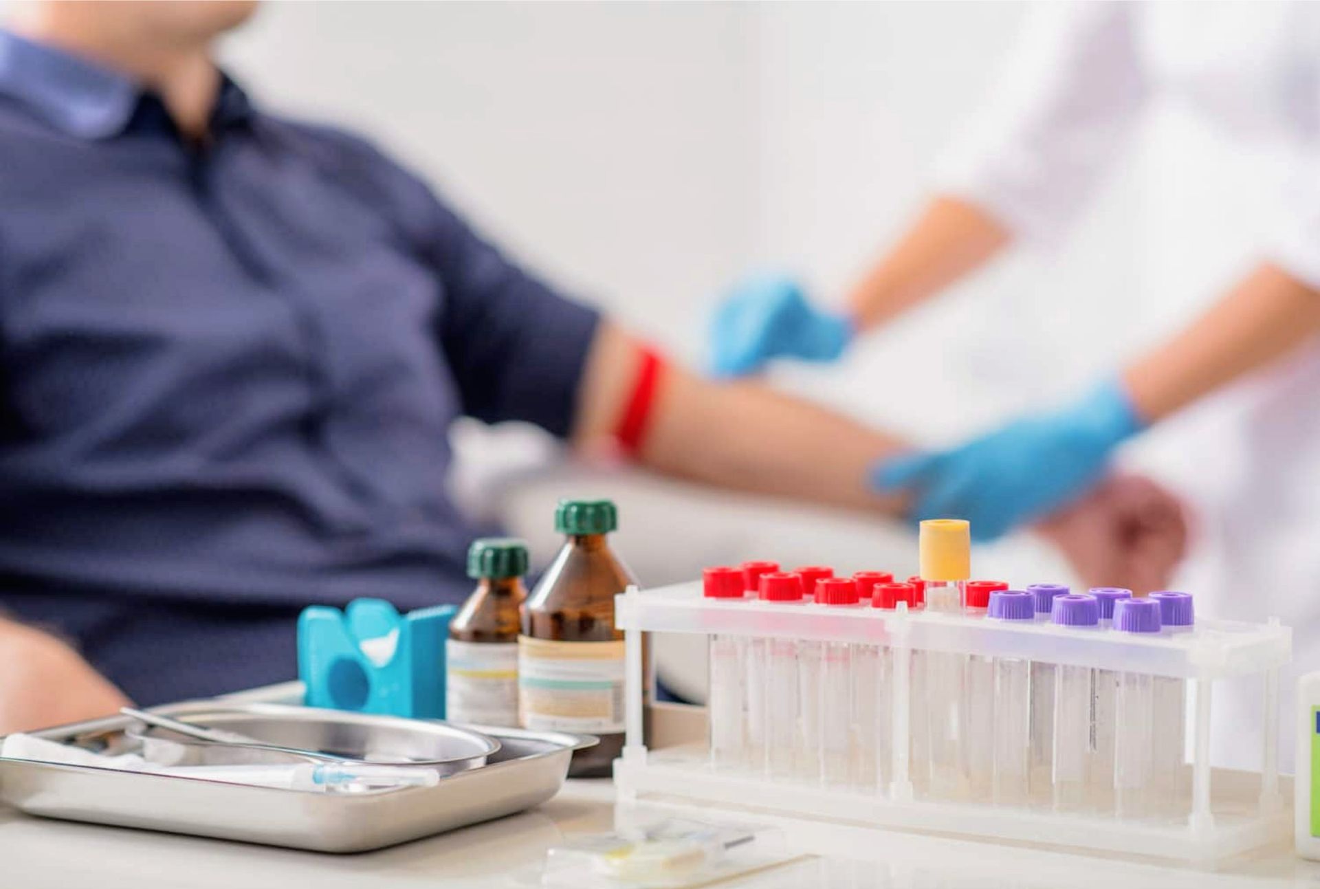 Person getting blood drawn by a healthcare worker; vials and medical supplies on a table.