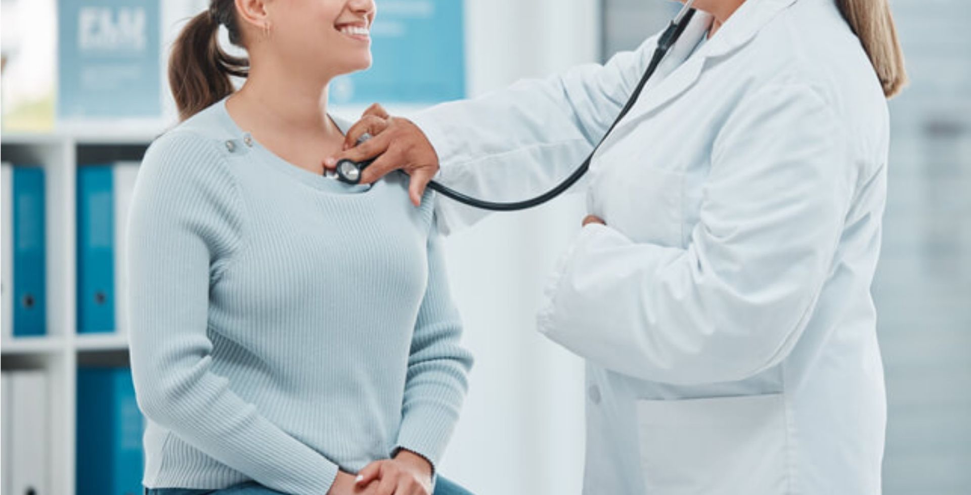 Doctor listening to patient's chest with a stethoscope in a medical office.