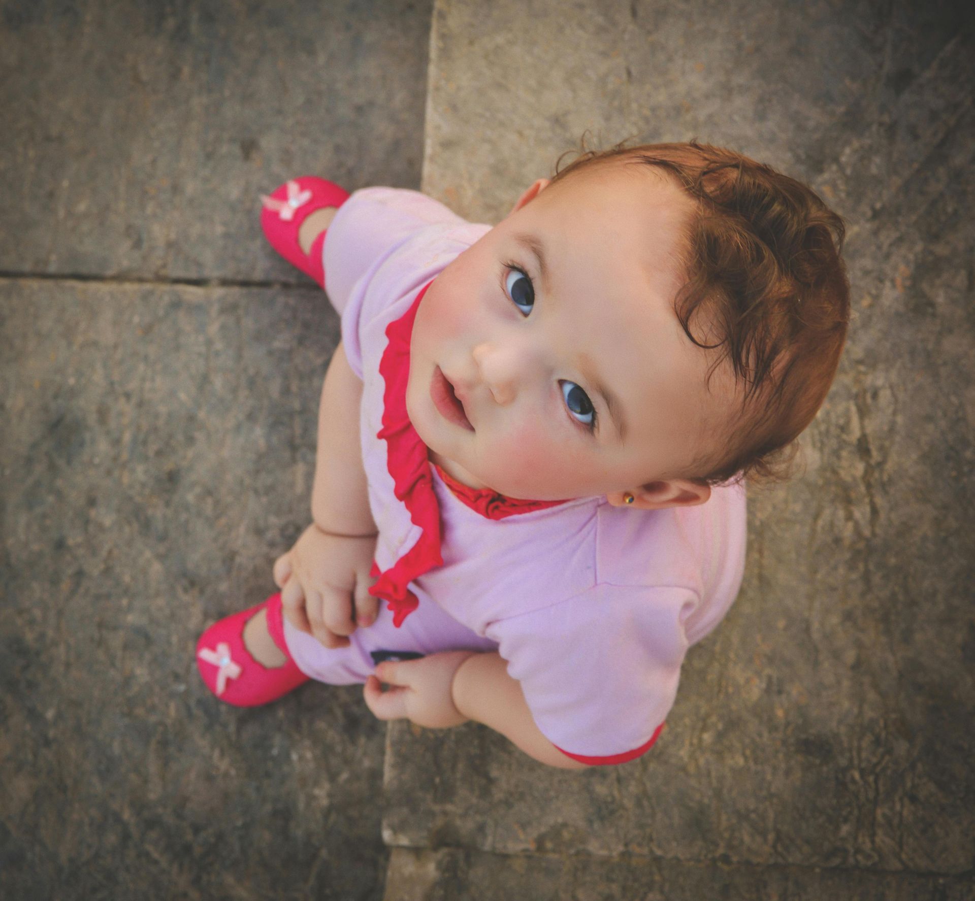 A baby in a pink outfit is looking up at the camera