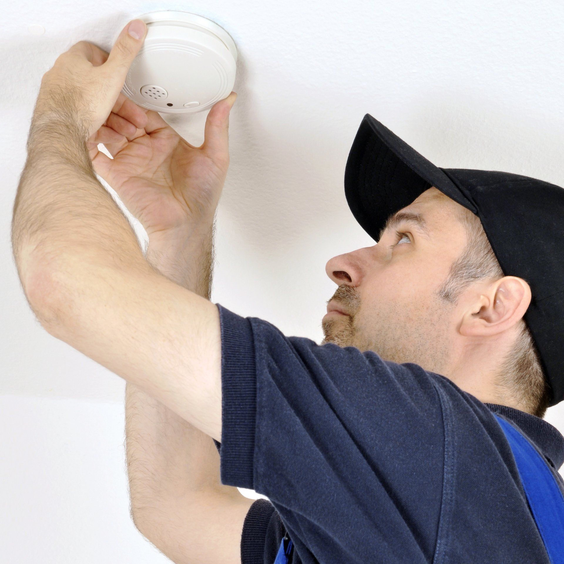 Technicien installant un détecteur de fumée au plafond dans le cadre d’un dispositif de sécurité incendie.