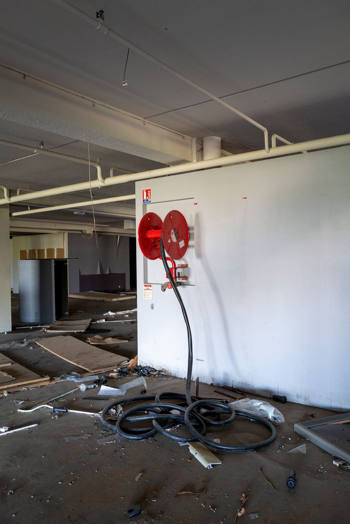 Poteau incendie mural RIA endommagé dans un bâtiment à l’abandon, avec tuyau au sol et débris environnants.