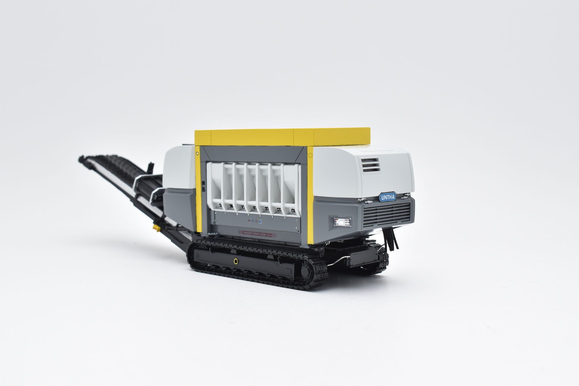 Een industriële machine op rupsbanden, grijs en wit met een geel dak, verwerkt materialen.