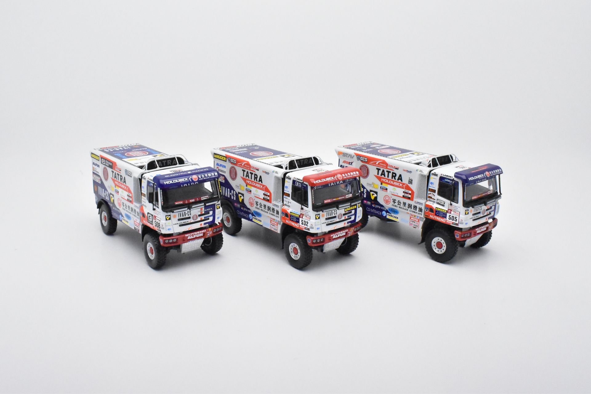 Drie wit-rode racetrucks met kleurrijke stickers op een witte achtergrond.