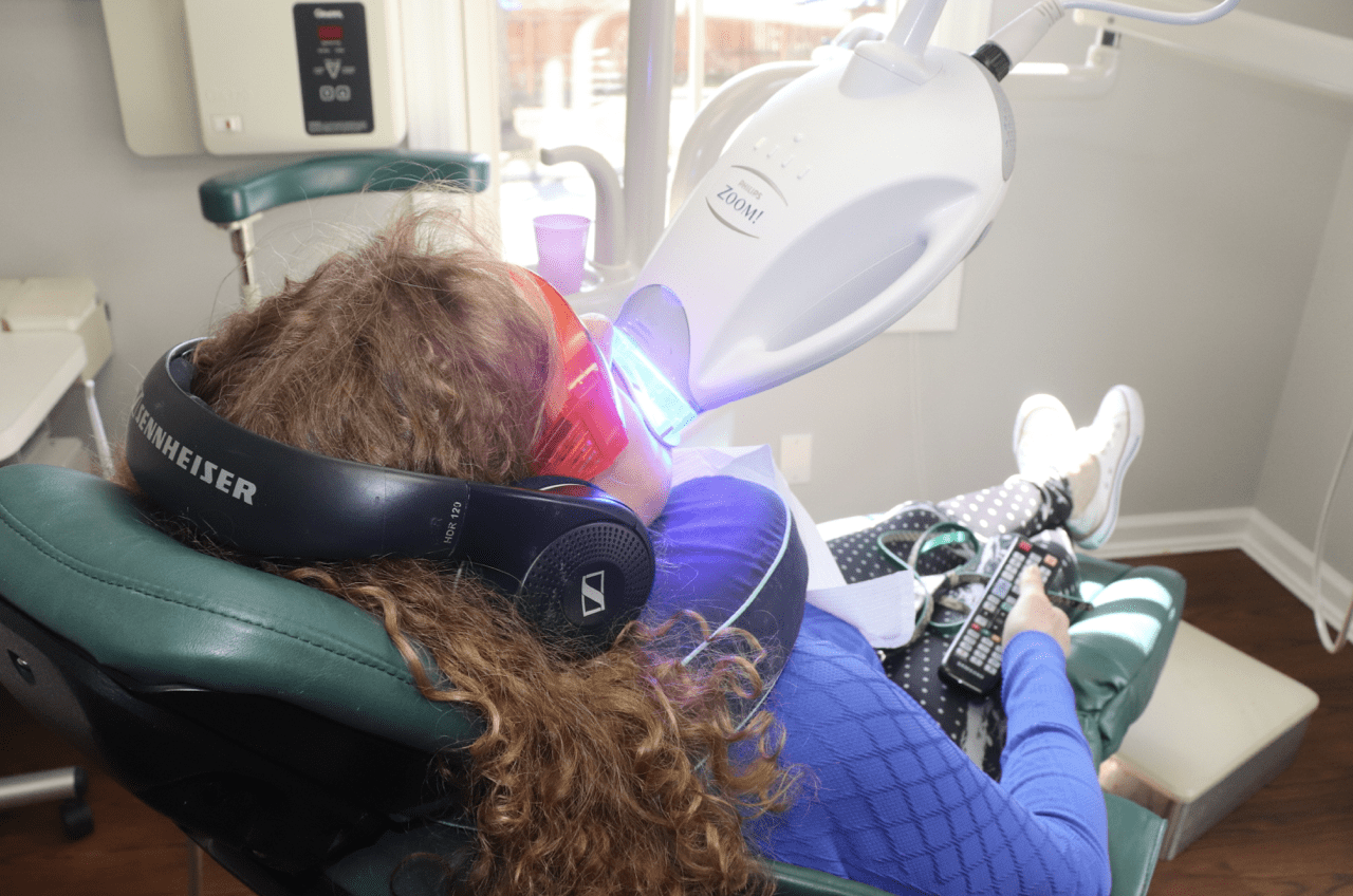 A woman is sitting in a dental chair getting her teeth whitened