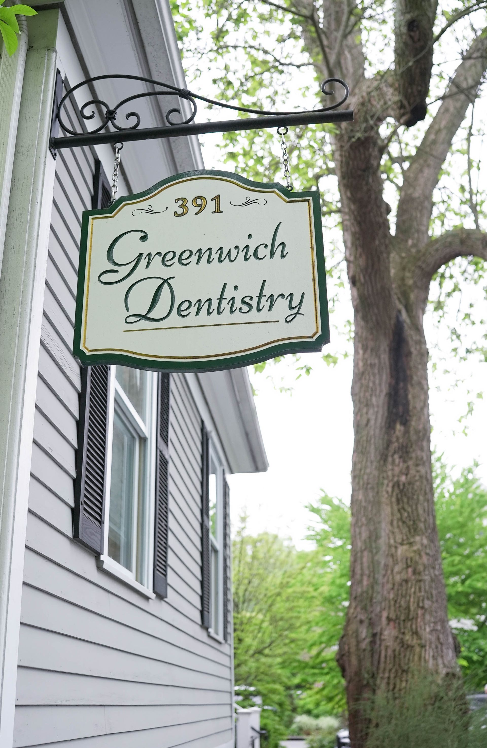 A sign for greenwich dentistry hangs from the side of a building