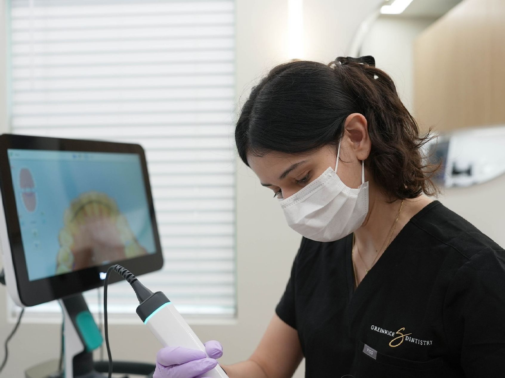 A woman wearing a mask and gloves is using a machine in a dental office