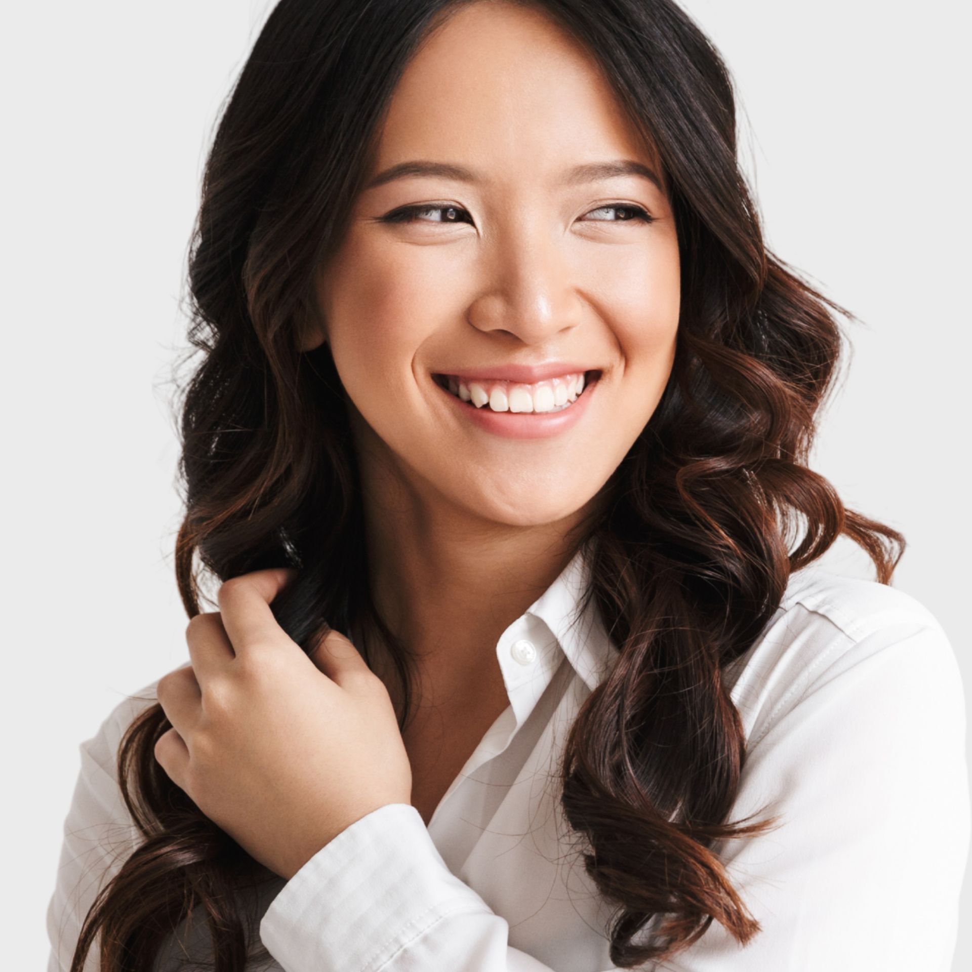 A woman in a white shirt is smiling and holding her hair
