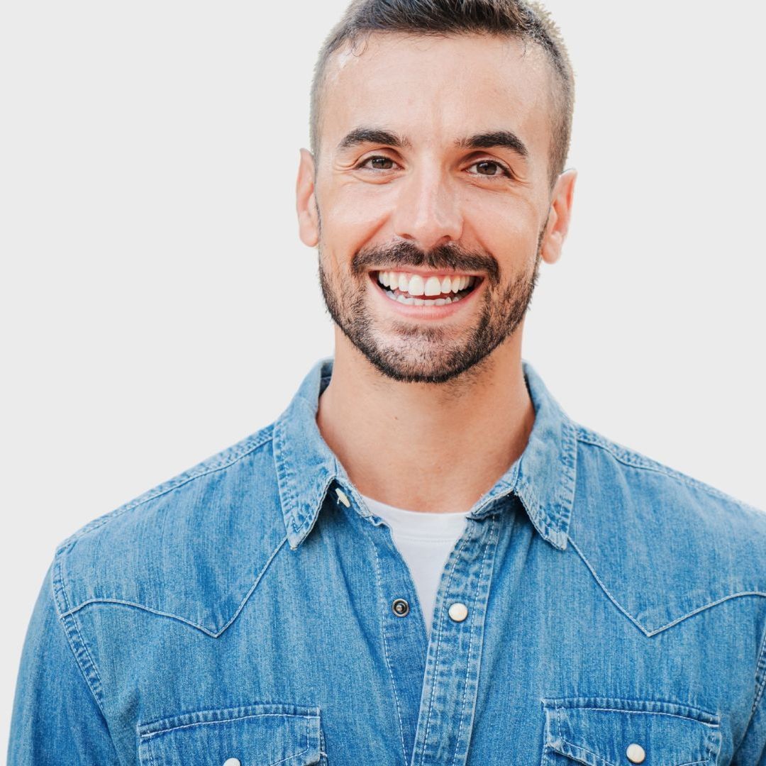 A man with a beard is wearing a denim shirt and smiling