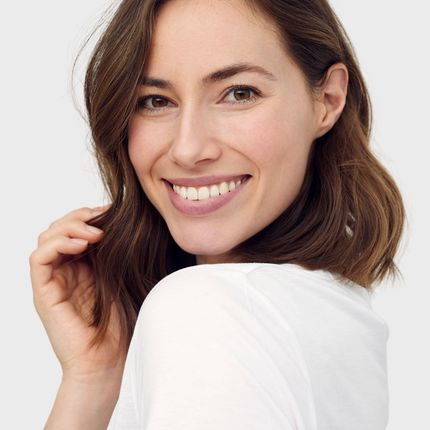 A woman in a white shirt is smiling and looking over her shoulder