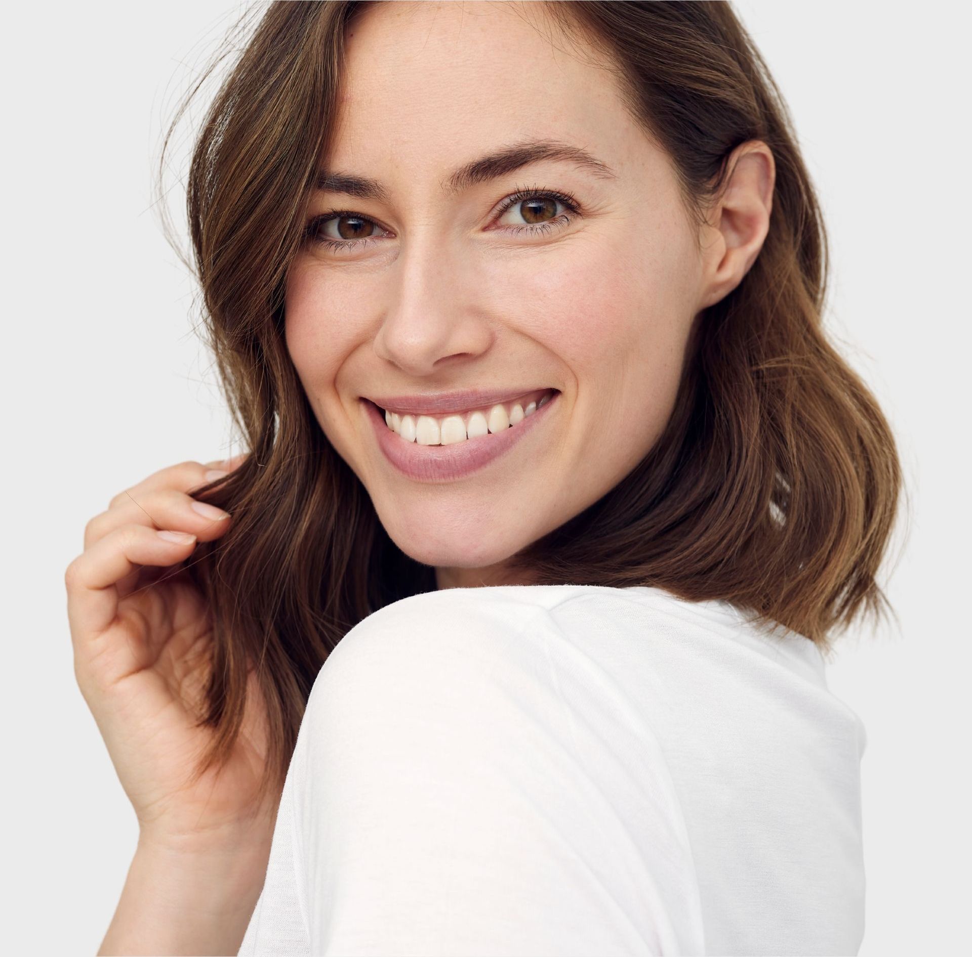 A woman in a white shirt is smiling and looking over her shoulder