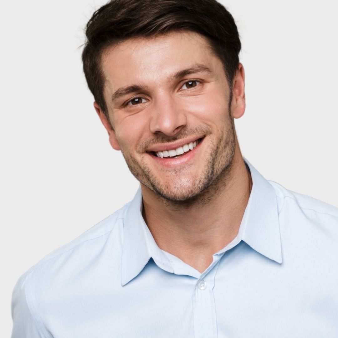 A man in a light blue shirt is smiling for the camera