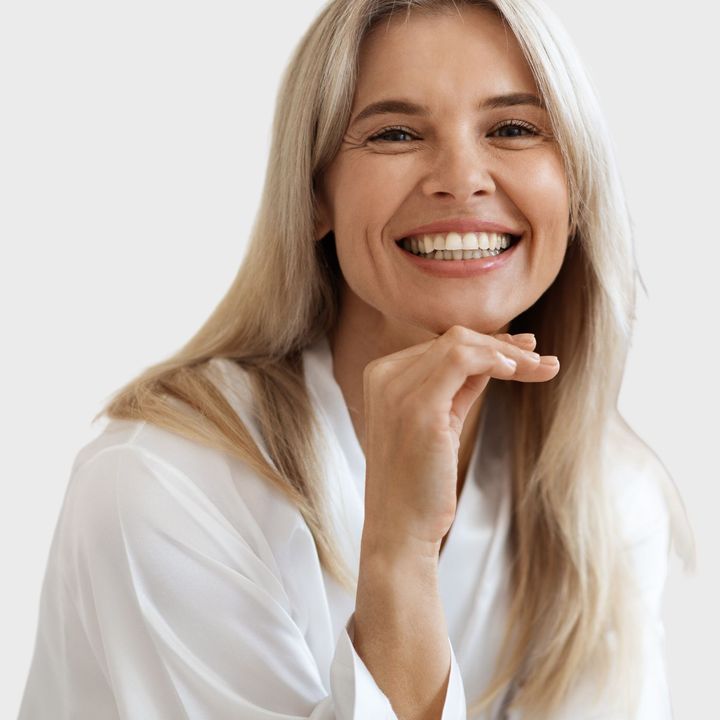A woman in a white shirt is smiling with her hand on her chin