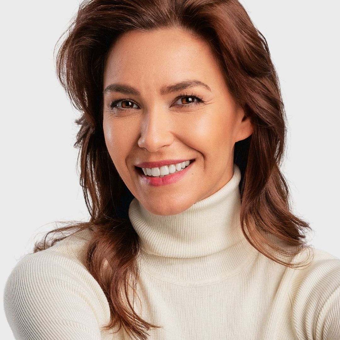 A woman wearing a white turtleneck sweater is smiling
