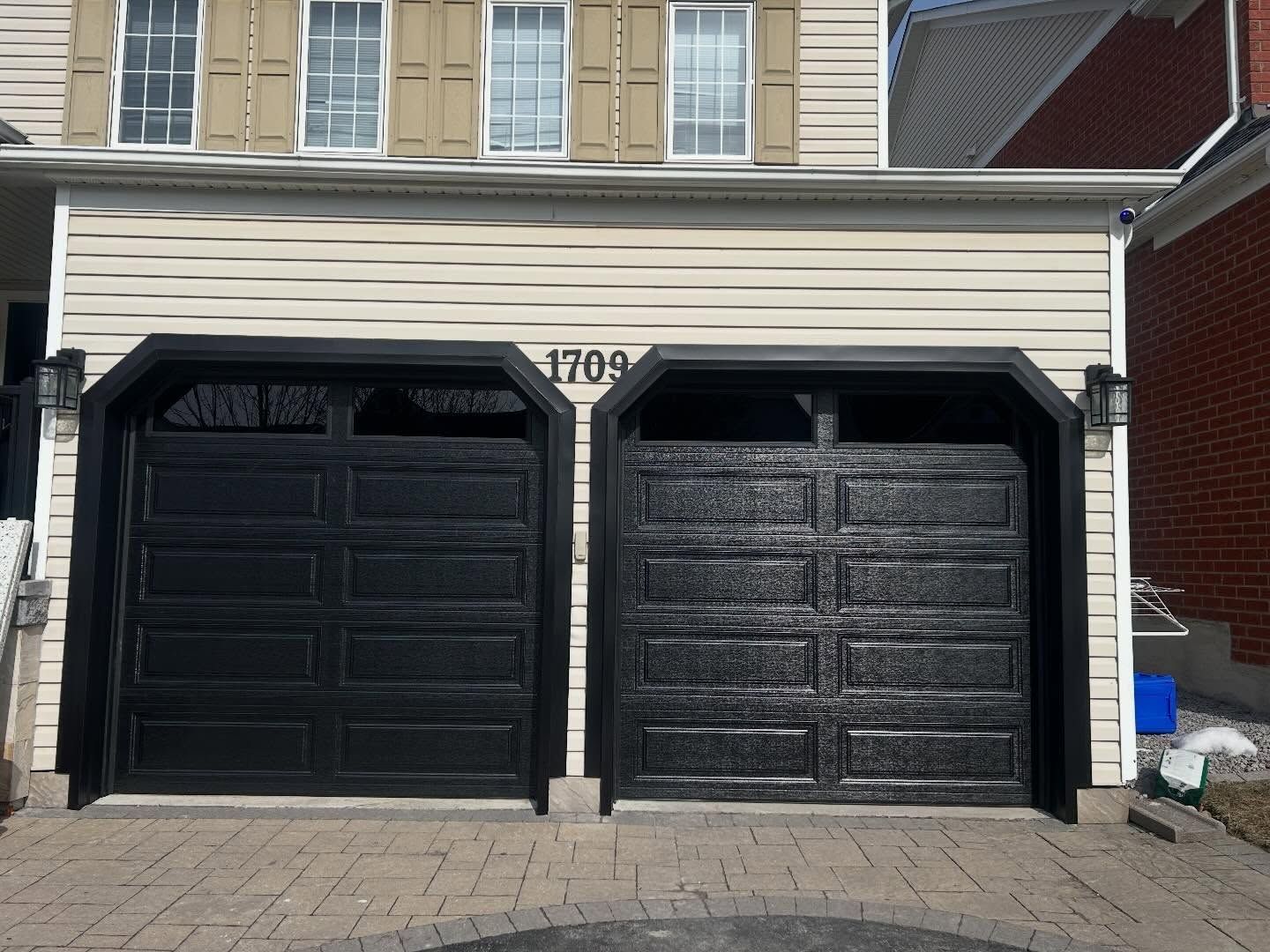 Two glossy black garage doors on a light beige house with the number 1709 displayed above them.