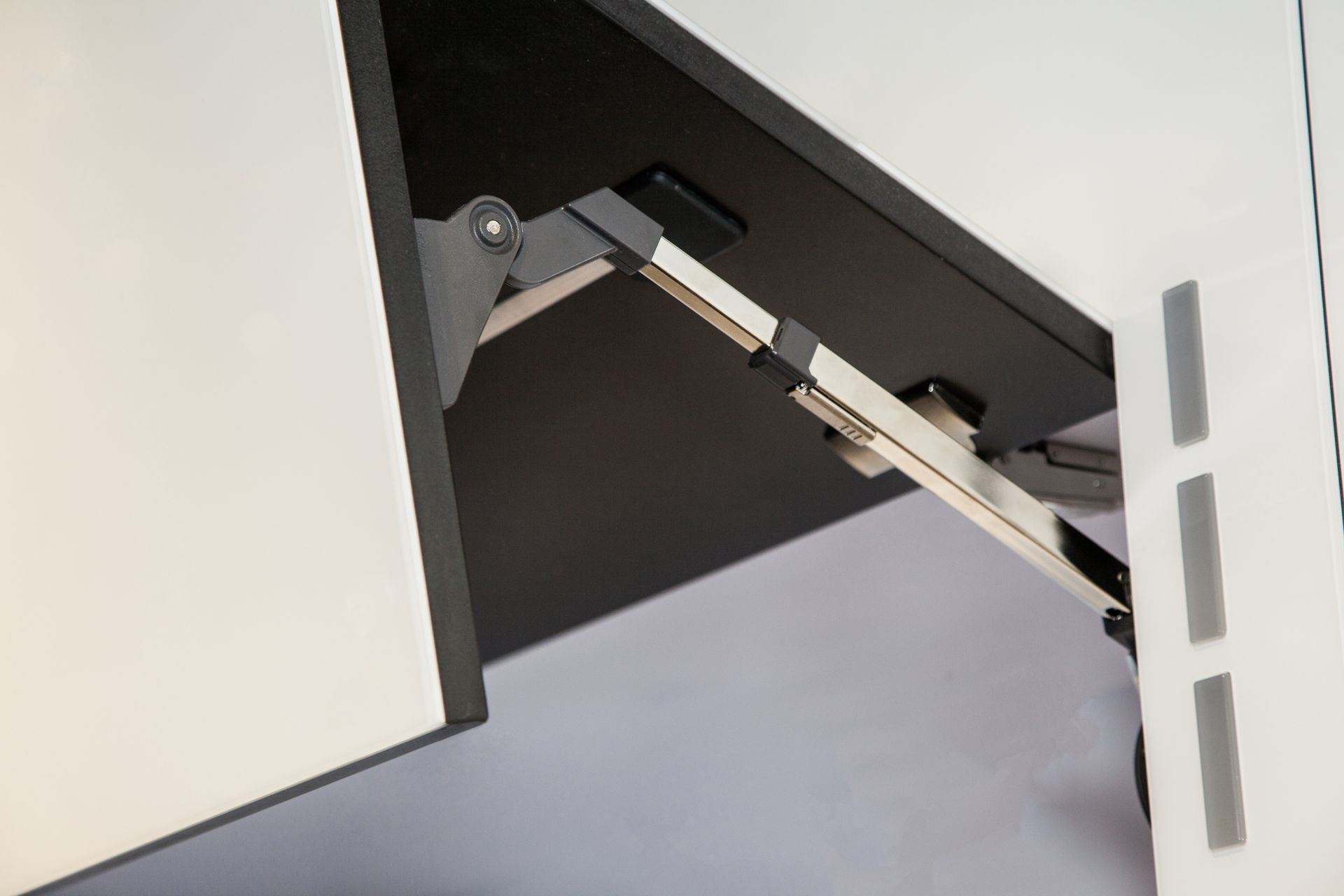 A metal kitchen cabinet hinge mechanism holding a white cupboard door partially open.