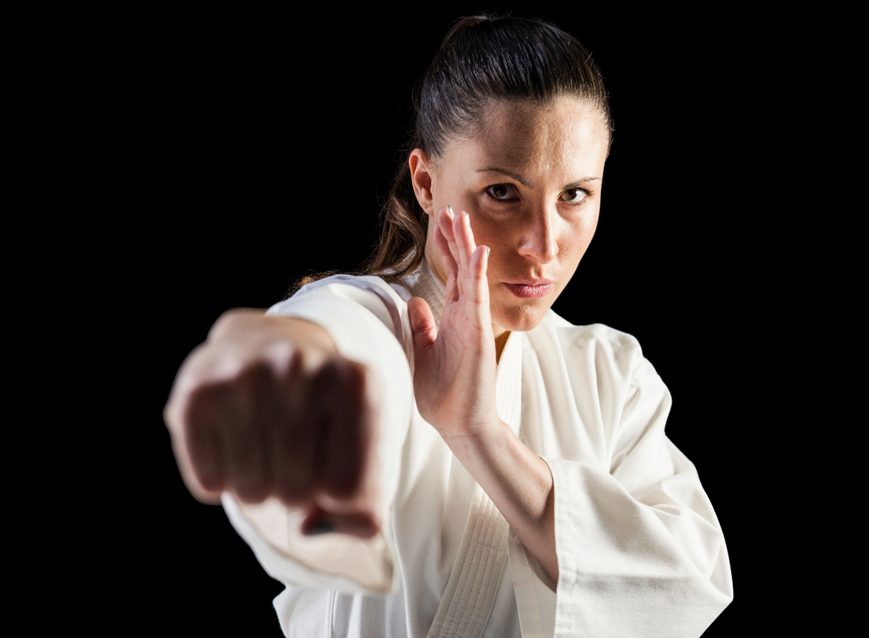 A woman in a white karate uniform is making a fist in the air.