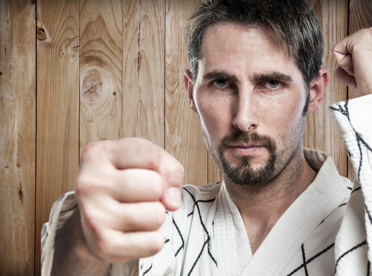 A man in a karate uniform is pointing at the camera