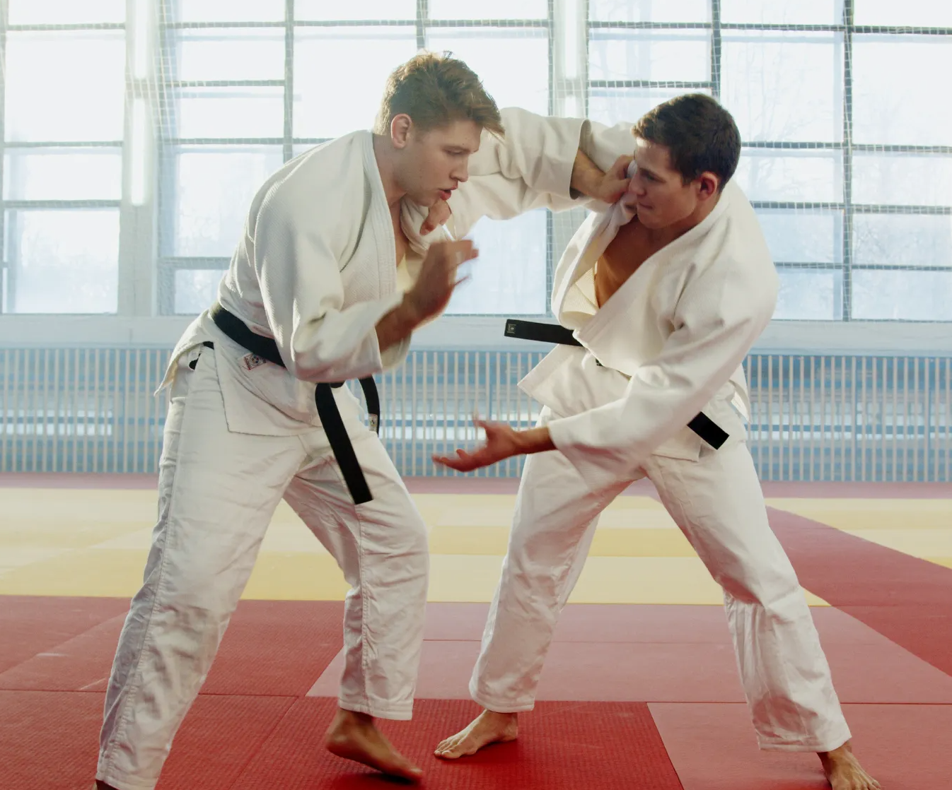 Two men are practicing judo on a mat in a gym.