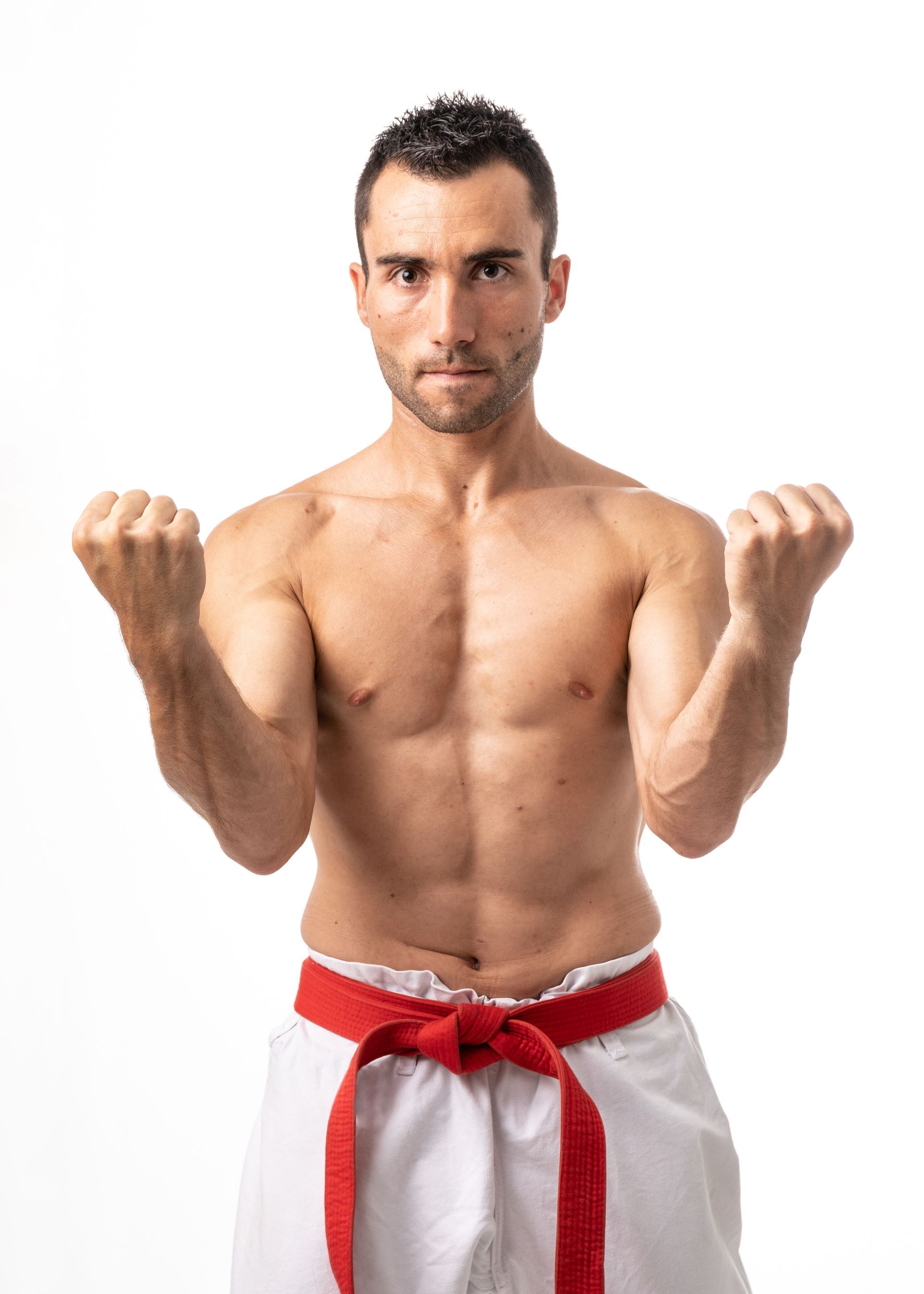 A shirtless karate man with a red belt is standing with his fist in the air.