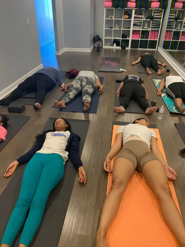 A group of people lying flat on their backs on yoga mats in a studio for a guided relaxation or meditation session.