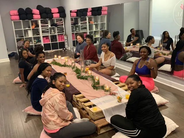 A group of people sit on floor cushions around a low, pallet-style dining table decorated with greenery and candles.