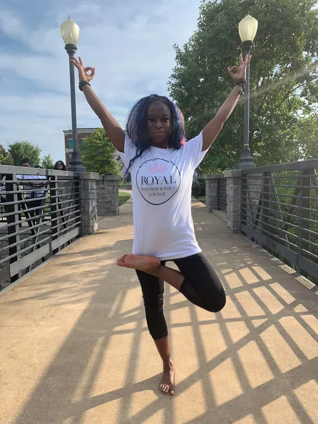 A person in a white t-shirt and black leggings balances in a tree yoga pose on a bridge between two street lamps.