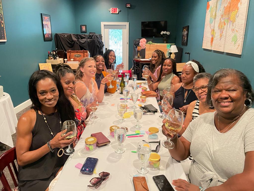 A group of people sitting at a long table, smiling and holding glasses during a celebratory dinner in a teal room.