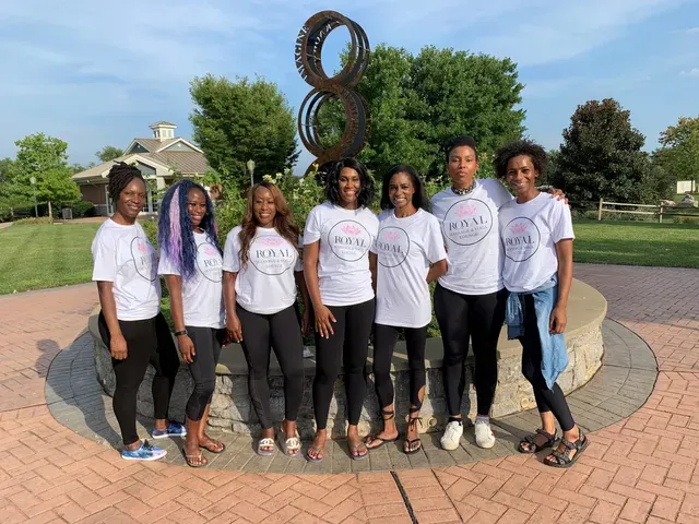 Eight people in matching white shirts pose in front of a metal sculpture shaped like the number eight in a park setting.