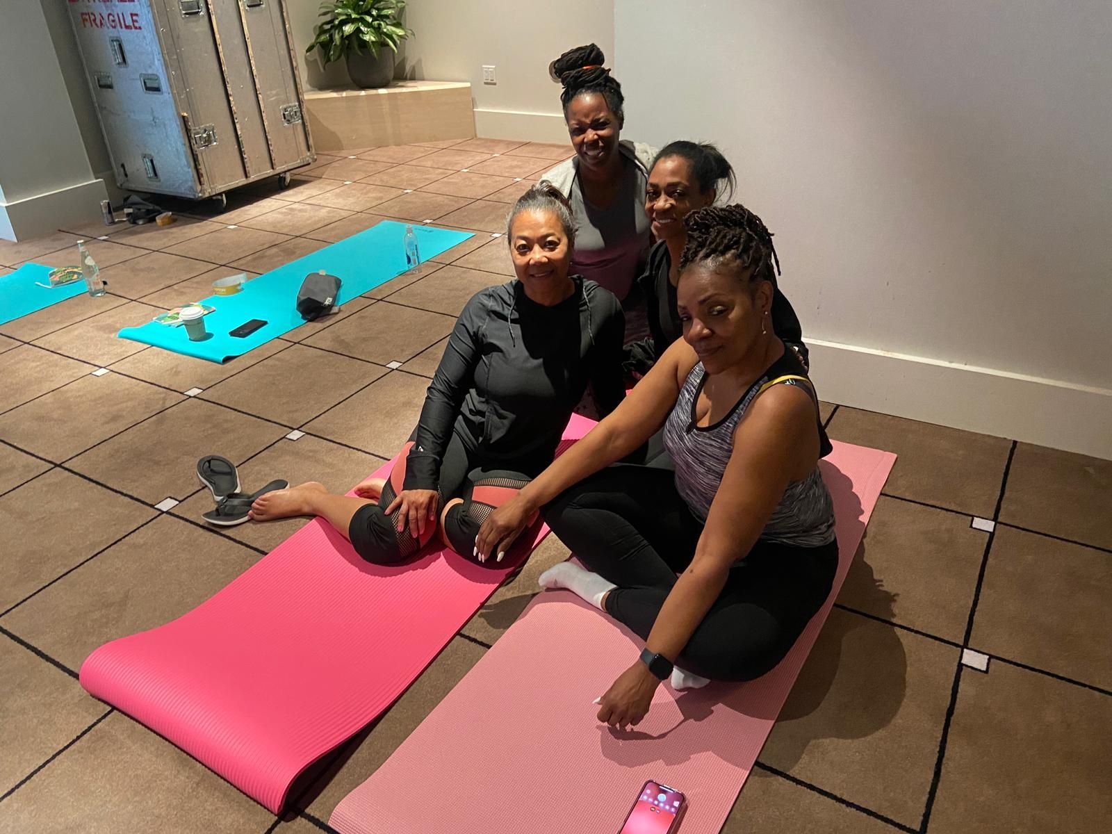 Four women in workout clothes on yoga mats in a room, smiling.