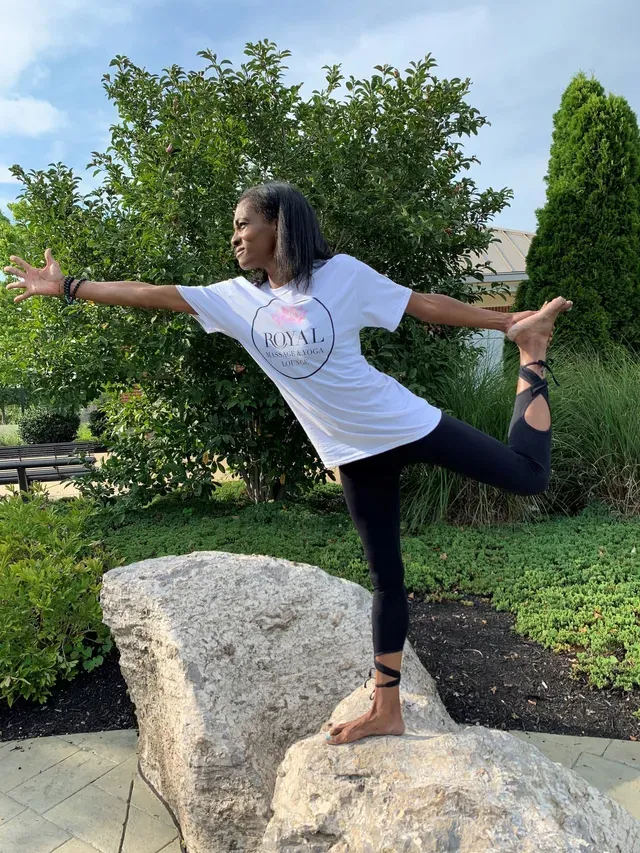 A person balances on a rock in a yoga pose, extending one arm forward and holding the opposite foot behind them.