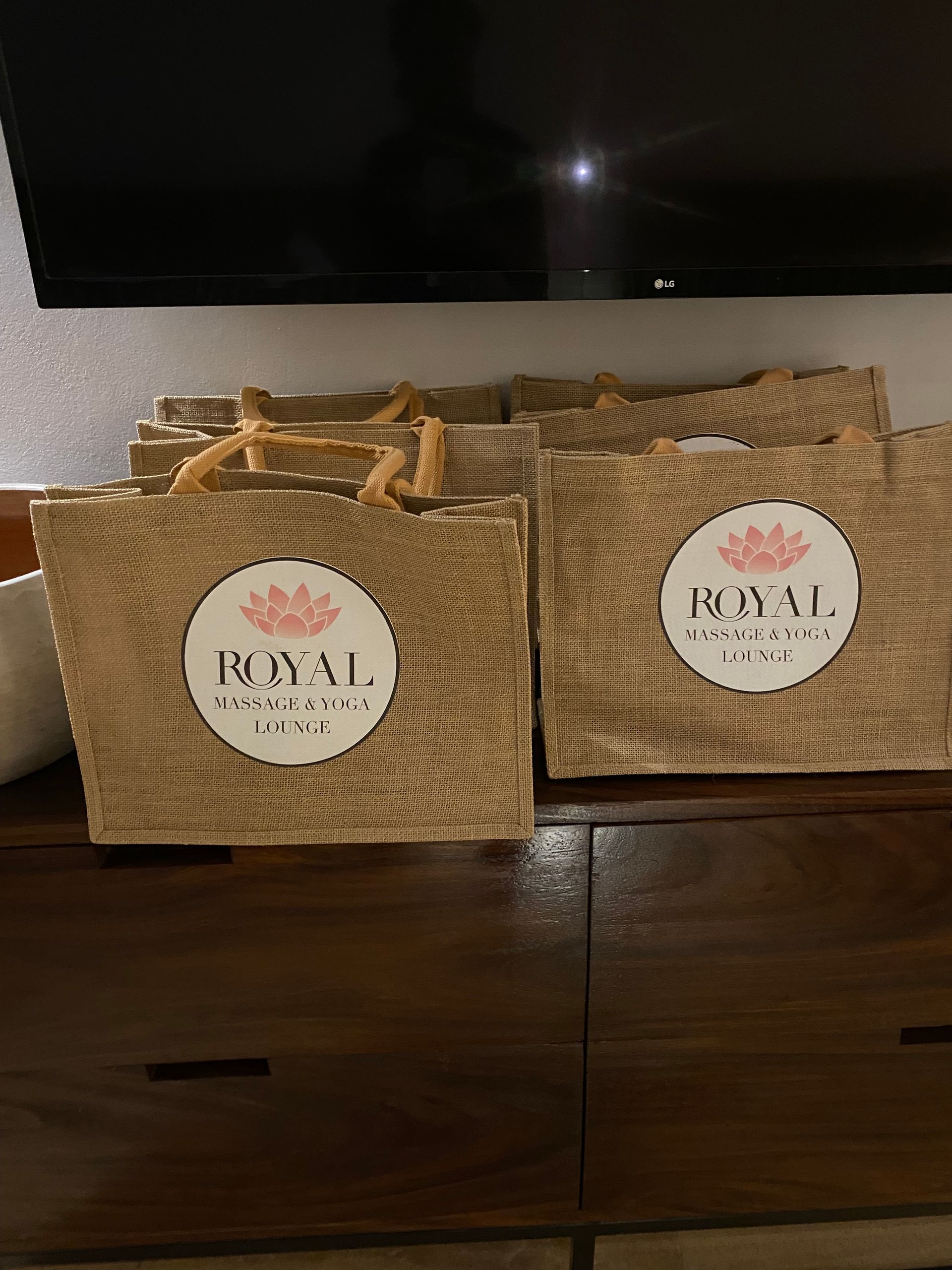 Multiple burlap gift bags with white circular labels featuring a pink logo and the text 