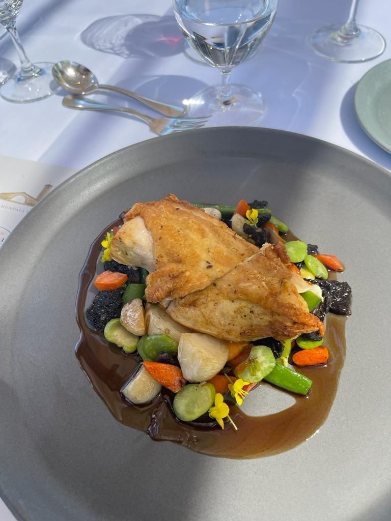 A crispy-skinned chicken breast served over sautéed vegetables and black forbidden rice with a dark brown sauce on a plate.