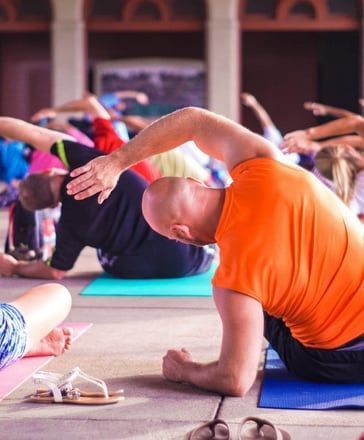 People in a group yoga or stretching class kneeling on colorful mats, reaching their arms overhead.