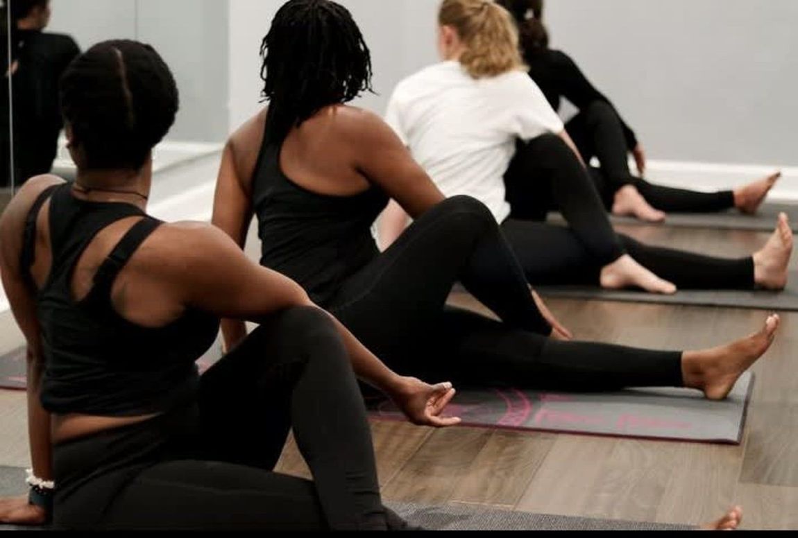 A group of people practicing a seated yoga spinal twist on mats in a studio.