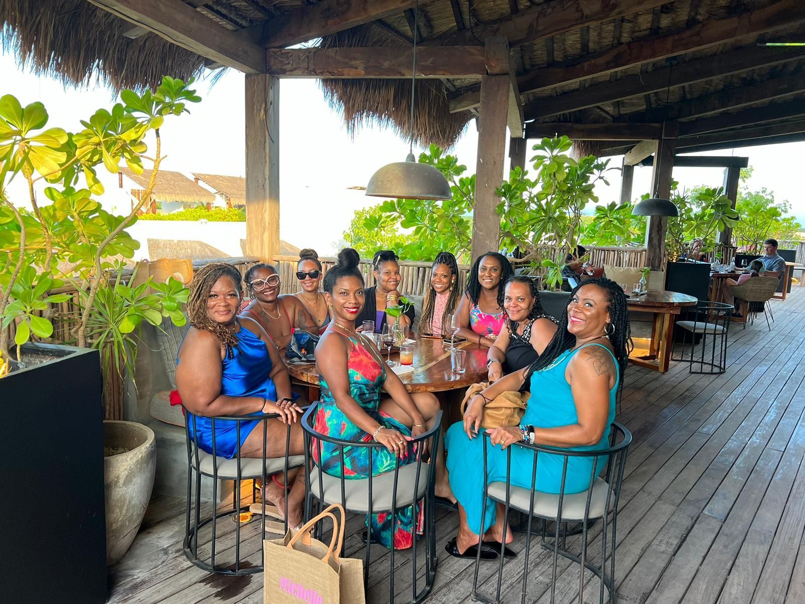 A group of people sitting at a table on a covered outdoor restaurant deck, smiling and posing for a photo.